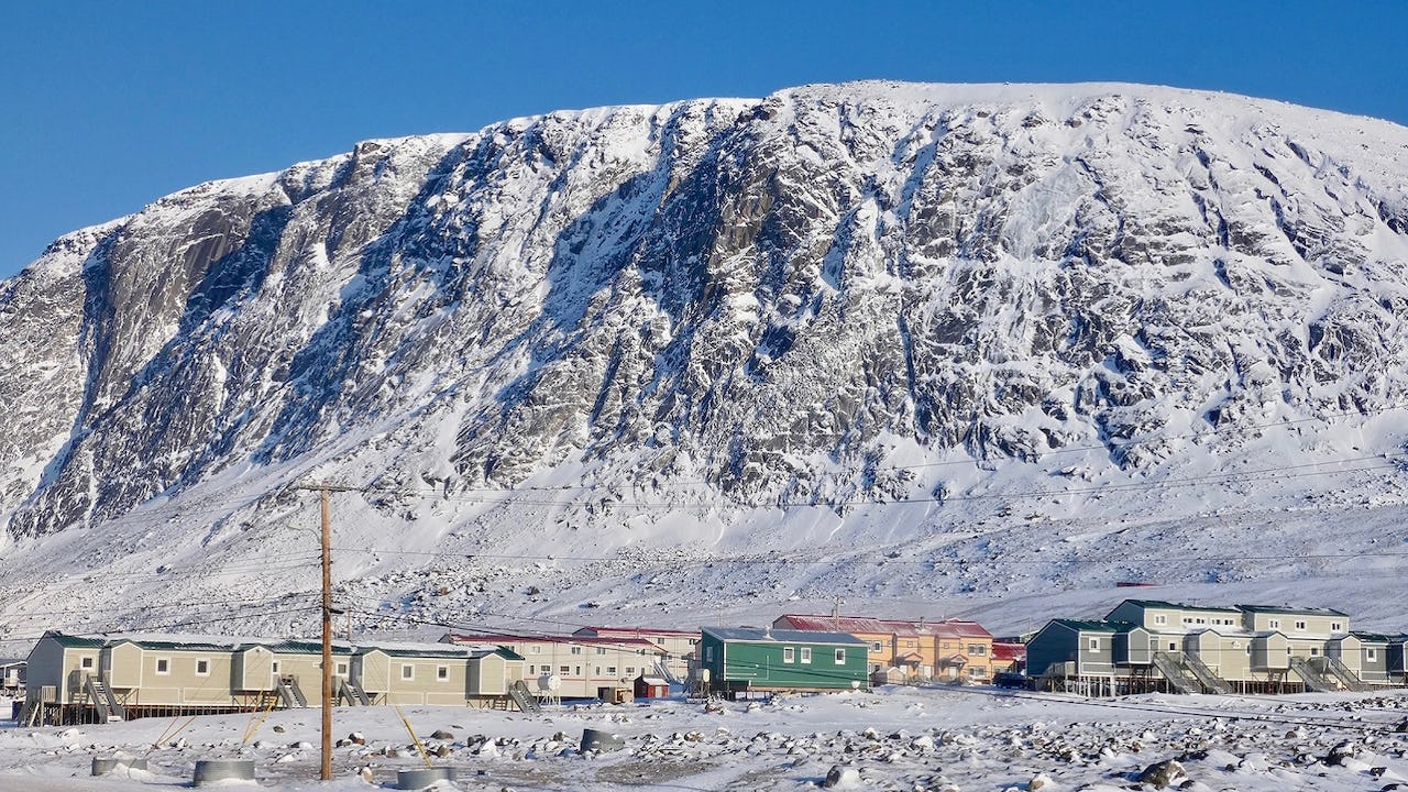 White and brown houses in Pangnirtung, Canada, near snowy mountain under blue sky during daytime