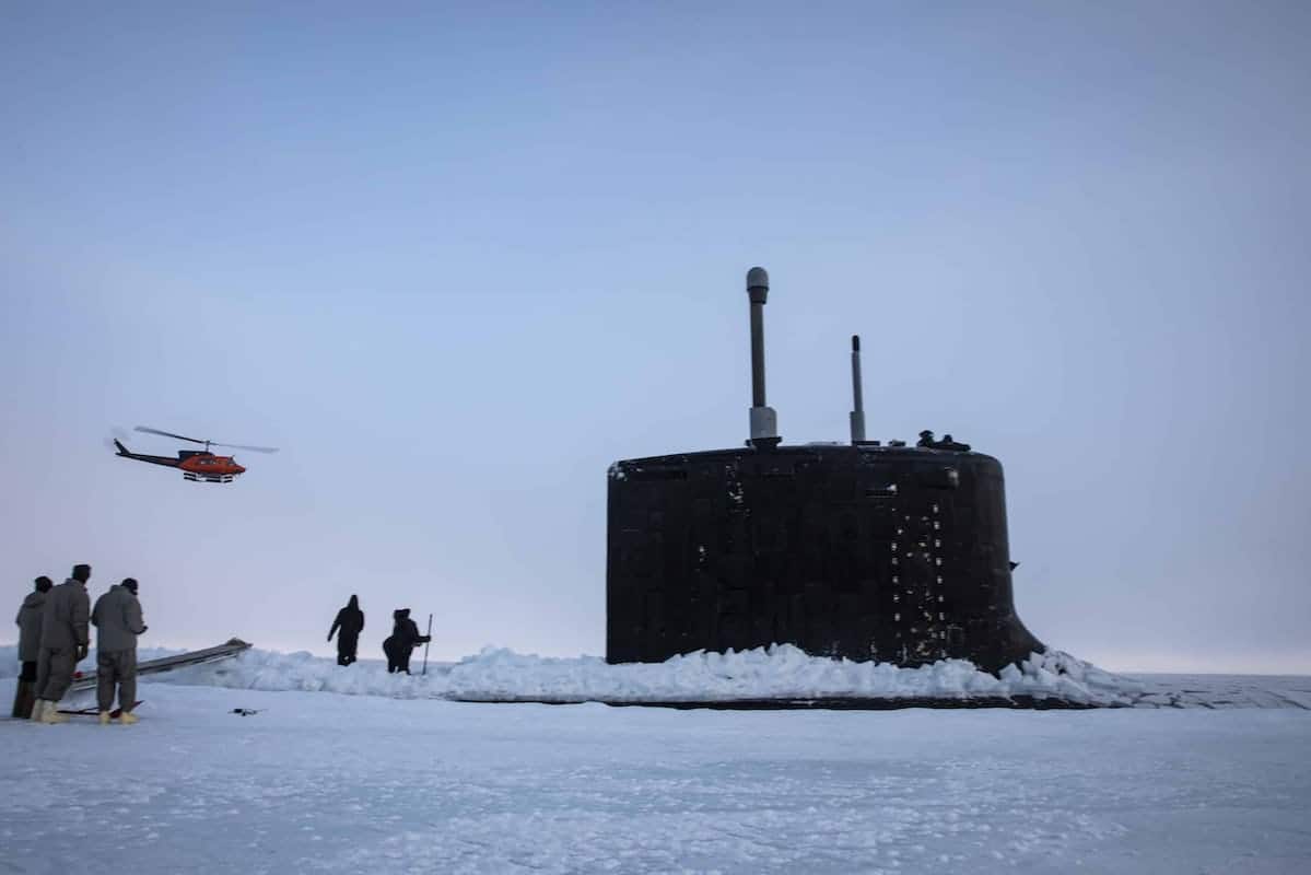 Submarine USS Illinois moors in sea ice with people standing outside and a red helicopter approaching