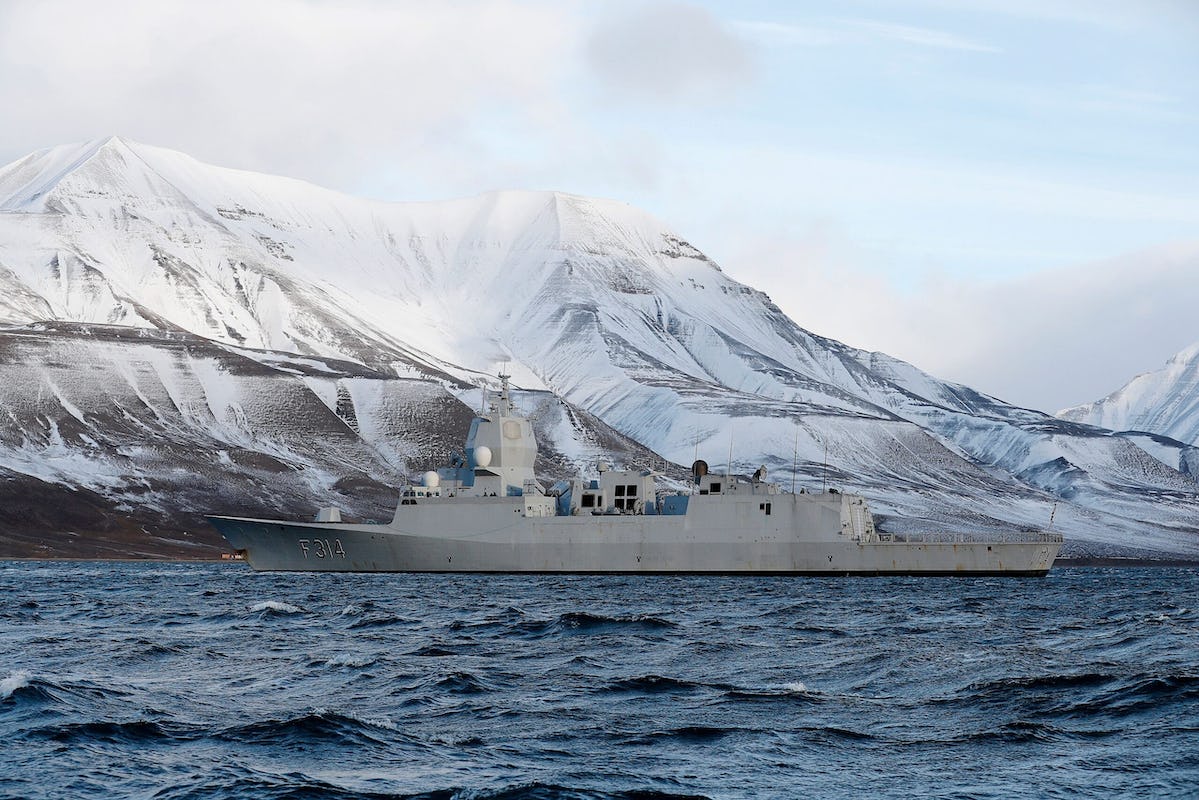 Grey Norwegian Navy Frigate KNM Thor Heyerdahl in sea off white mountains on Svalbard