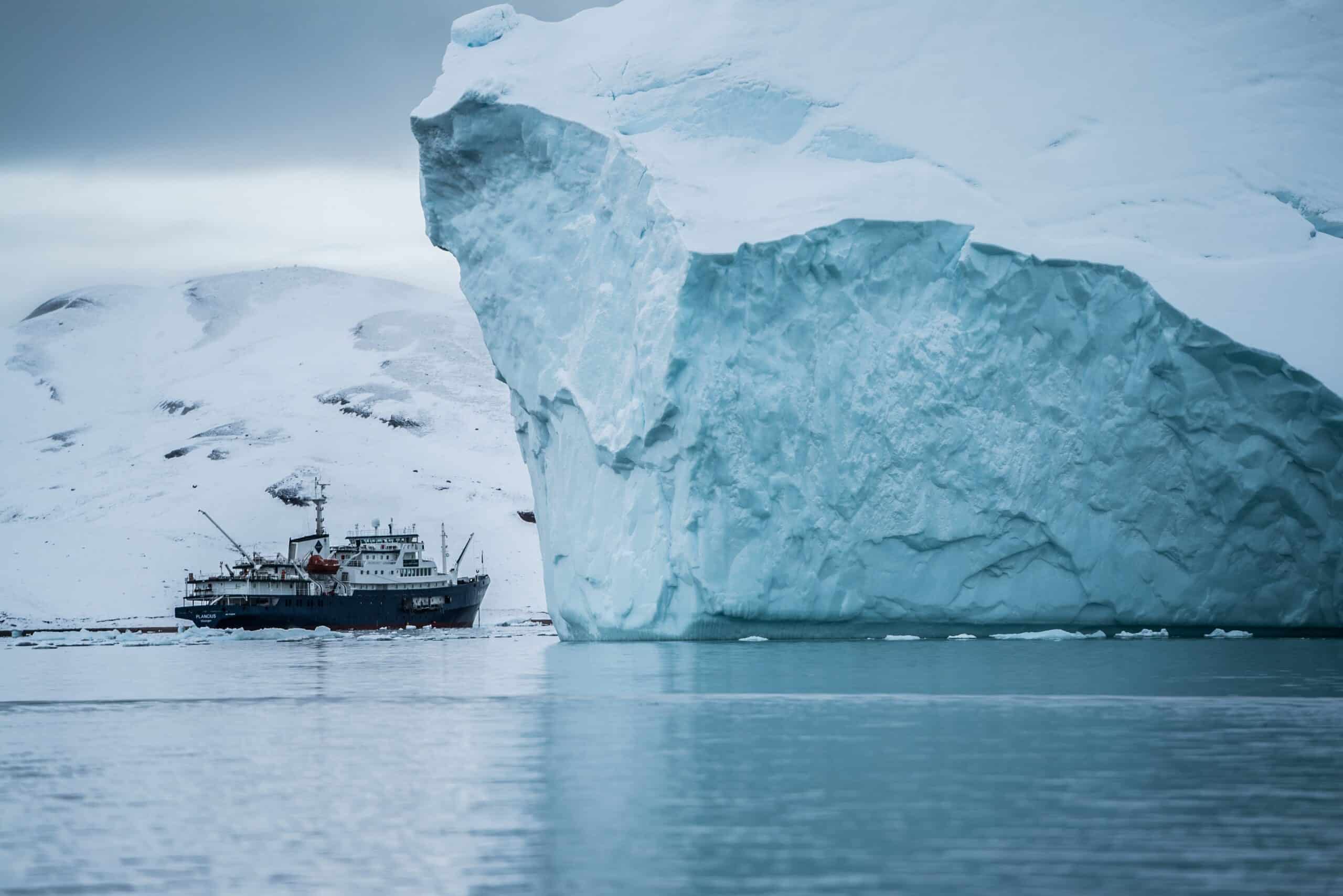 Boat beside iceberg with snow mountains in the back