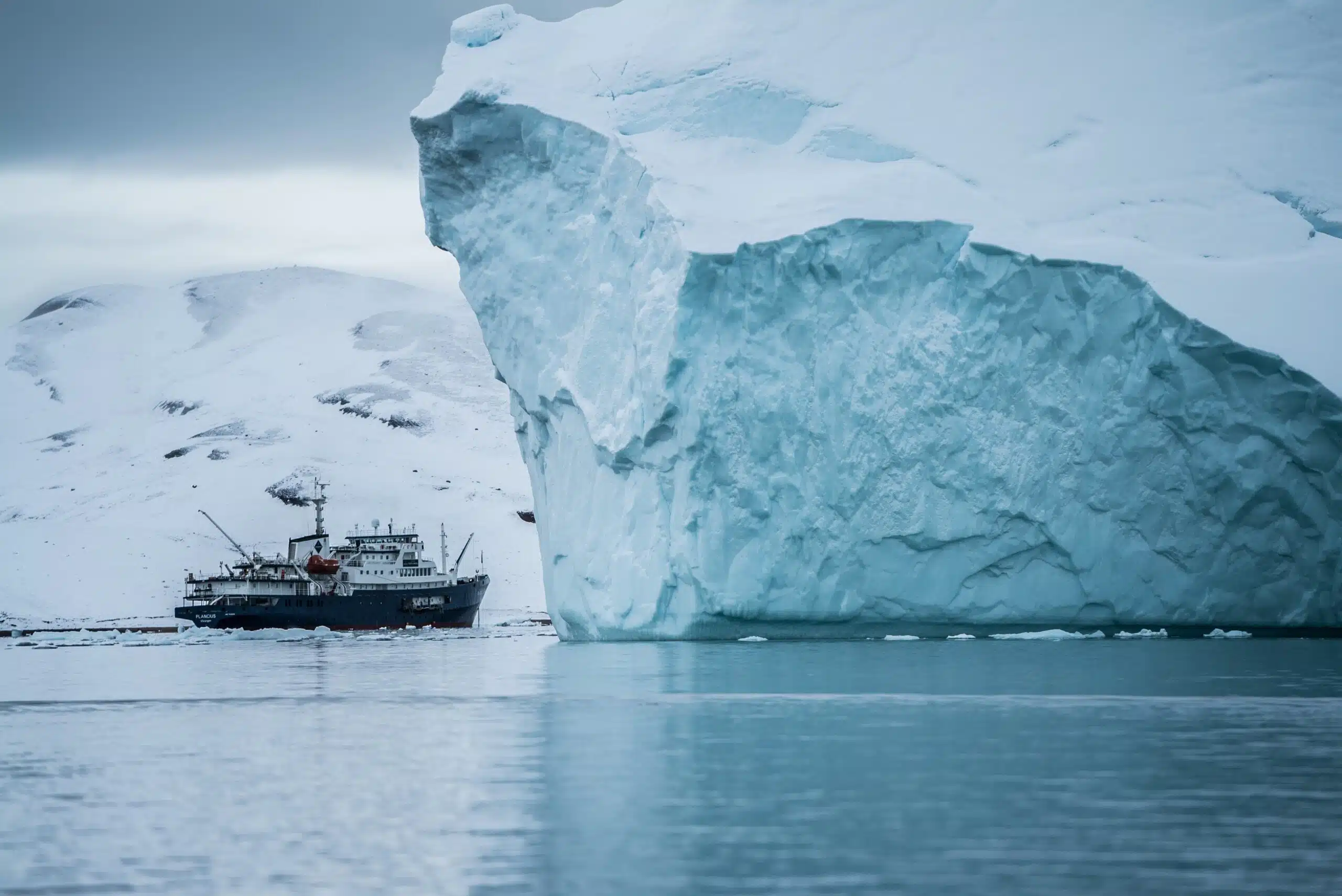 Boat beside iceberg with snow mountains in the back