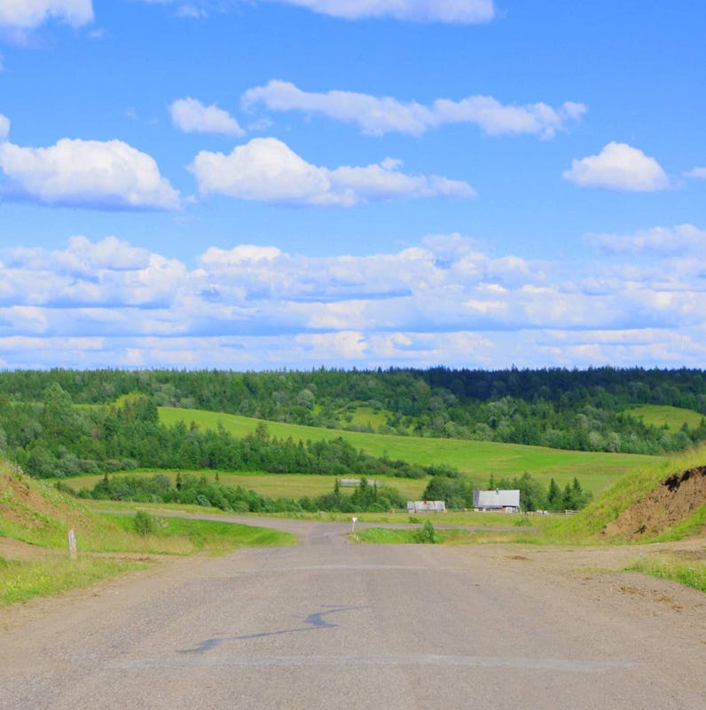 Paved street in the Komi Republic with a house and green hills in the back