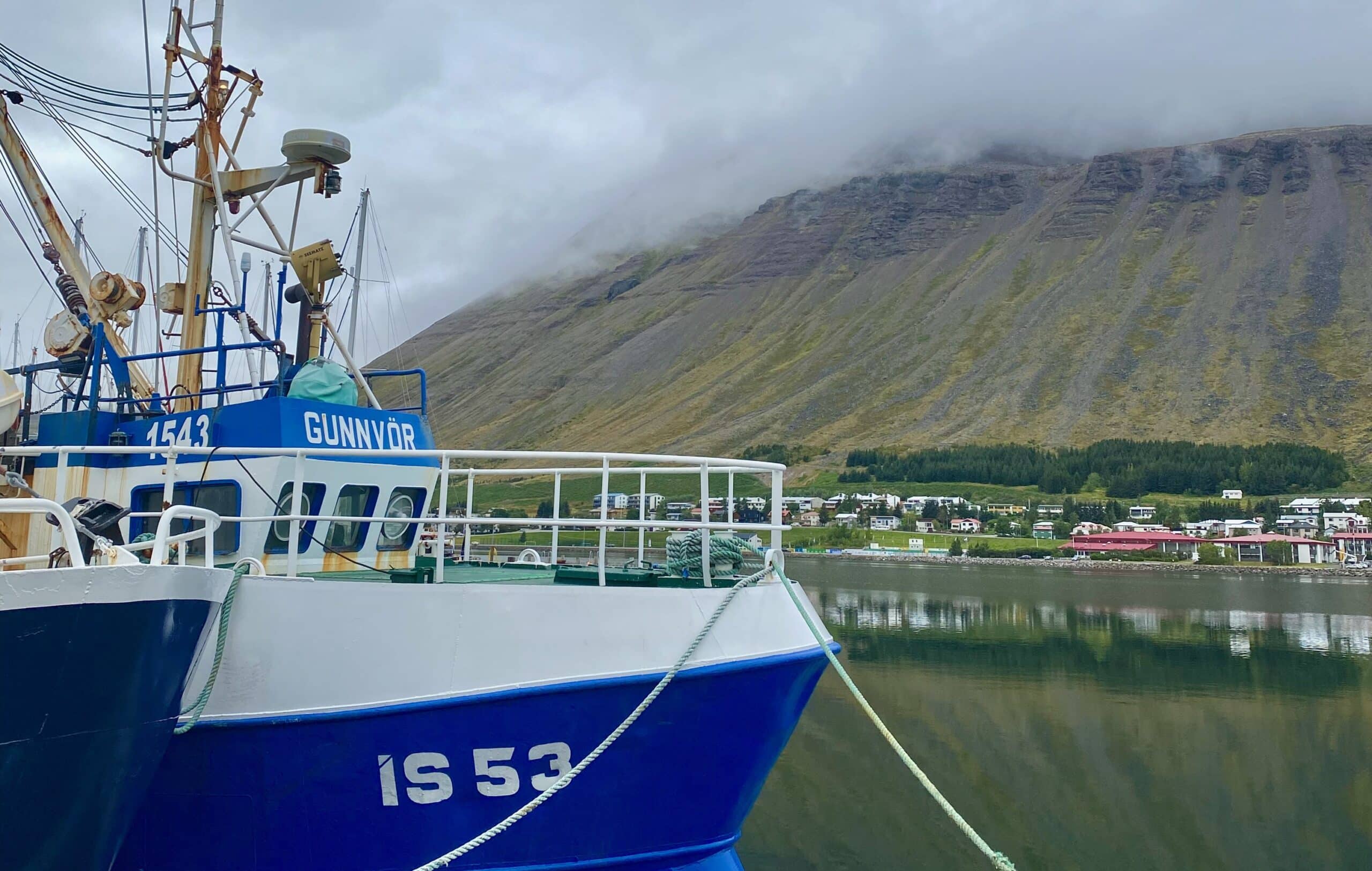 A fishing vessel connected to the pier with mooring ropes at the port of Isafjordur, with the port view at the background