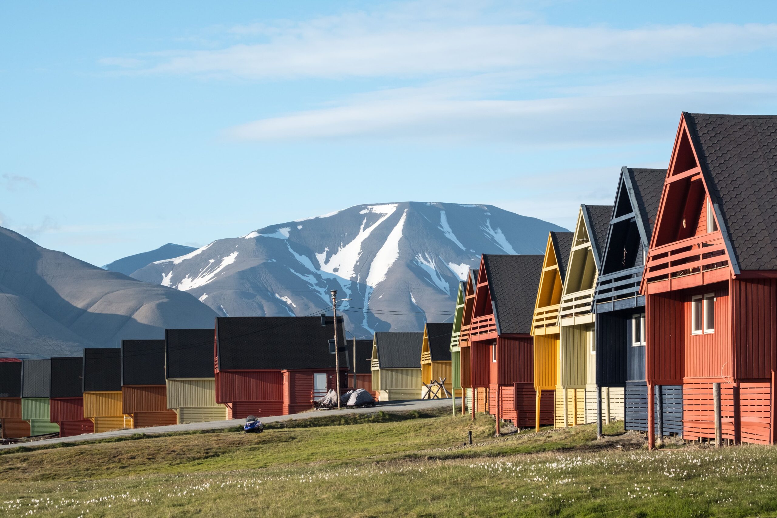 Many small colorful houses on a green lawn with a gray mountain and blue sky in the background
