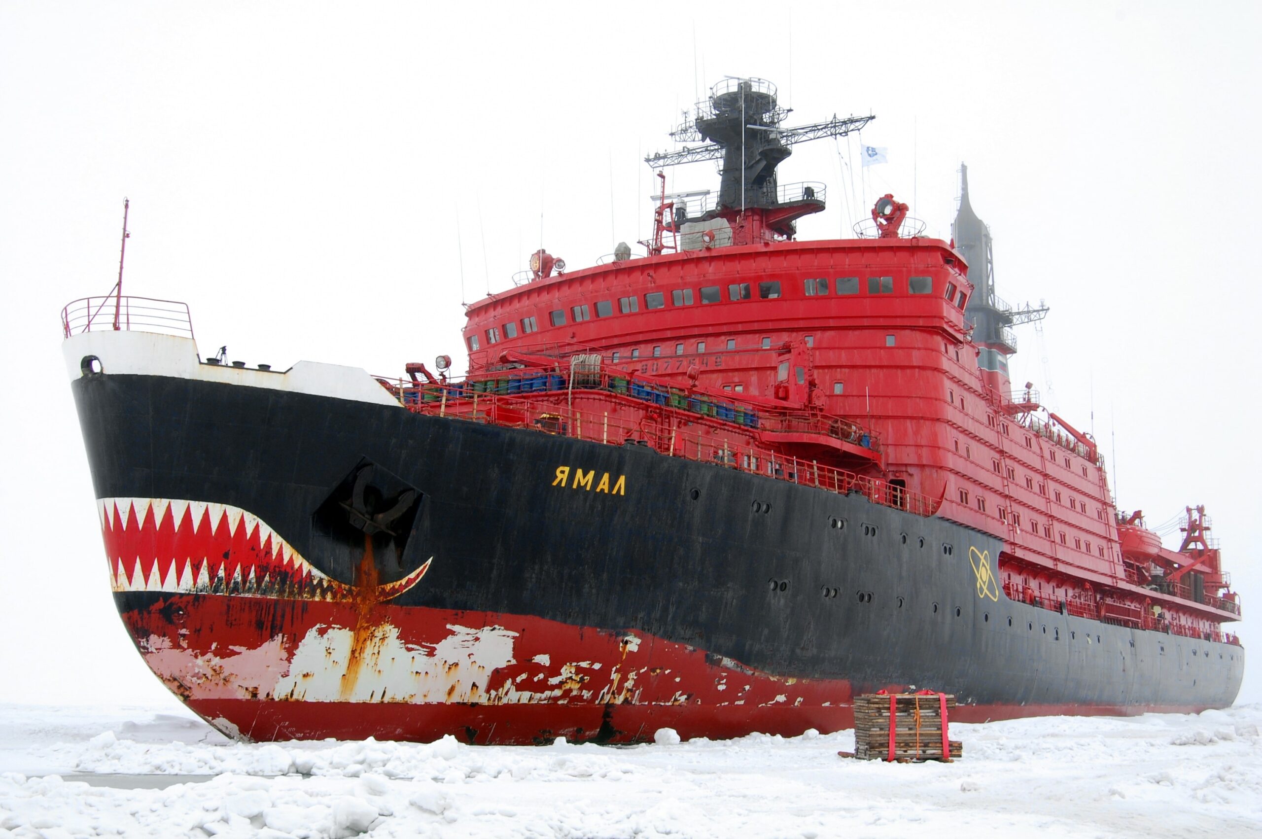 Massive red Russian nuclear icebreaker Yamal stands in Arctic sea ice. The ice-breaking ship has a mouth design on its front.