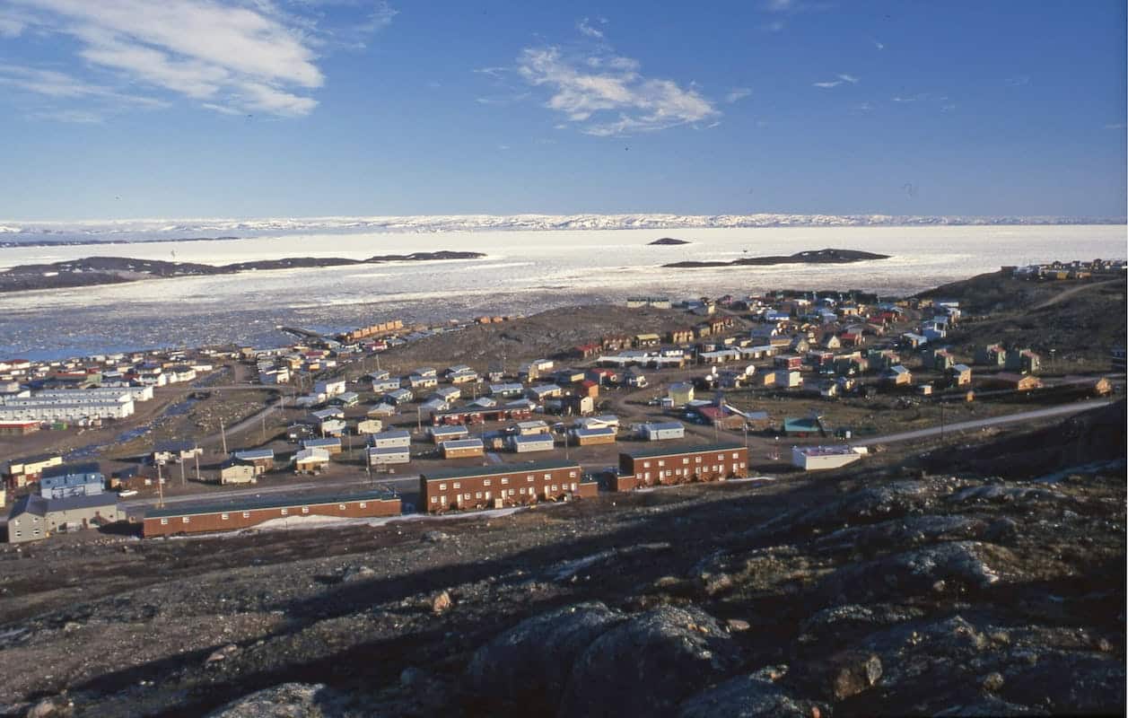 Houses on green tundra in the foreground with snow-covered mountains in the background