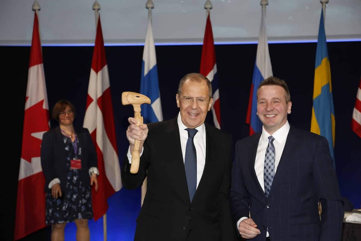 Russian Foreign Minister Sergey Lavrov holds wooden gavel next to Icelandic Foreign Minister Guðlaugur Þór Þórðarson at Arctic Council meeting in Reykjavik, Iceland, May 2021, background has flags of Canada, Denmark, Finland, Norway, Russia, Sweden and USA