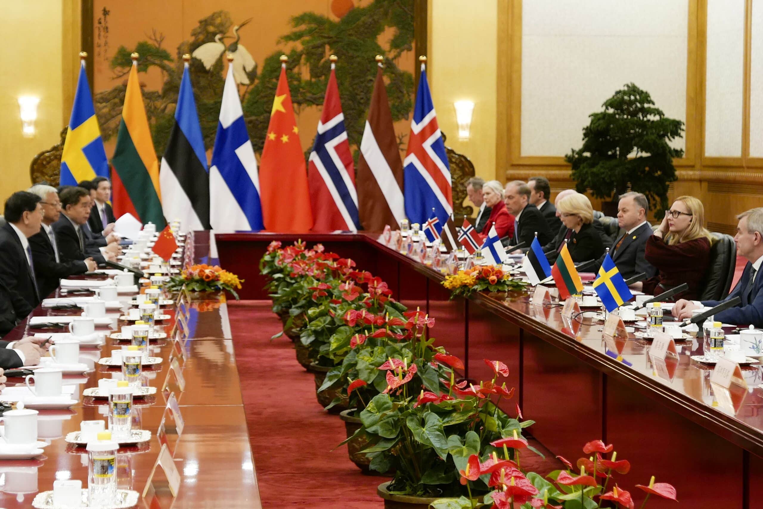 Politicians sitting around long tables facing each other with various flags in the background