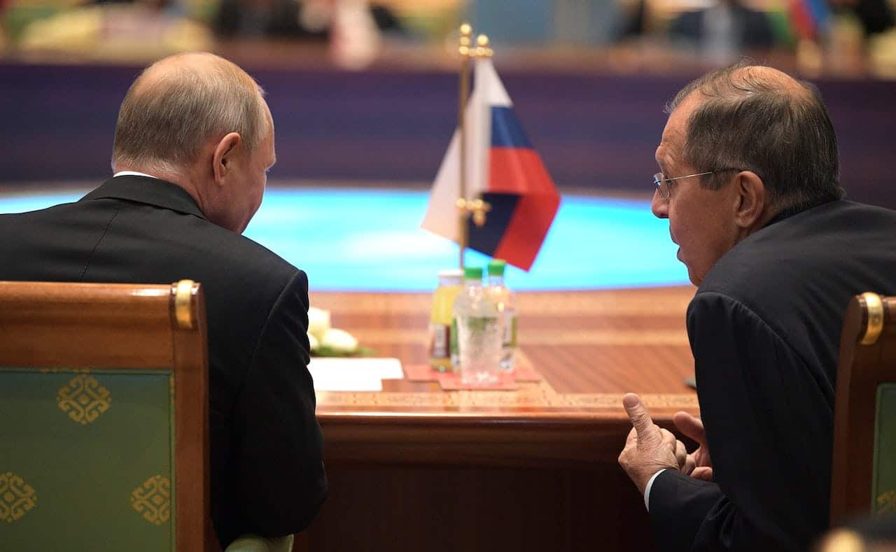 Russian President Vladimir Putin and Foreign Minister Sergey Lavrov sit with their backs to the camera at a table with the flag of the Russian Federation, before an expanded meeting of the CIS Heads of State Council in Turkmenistan