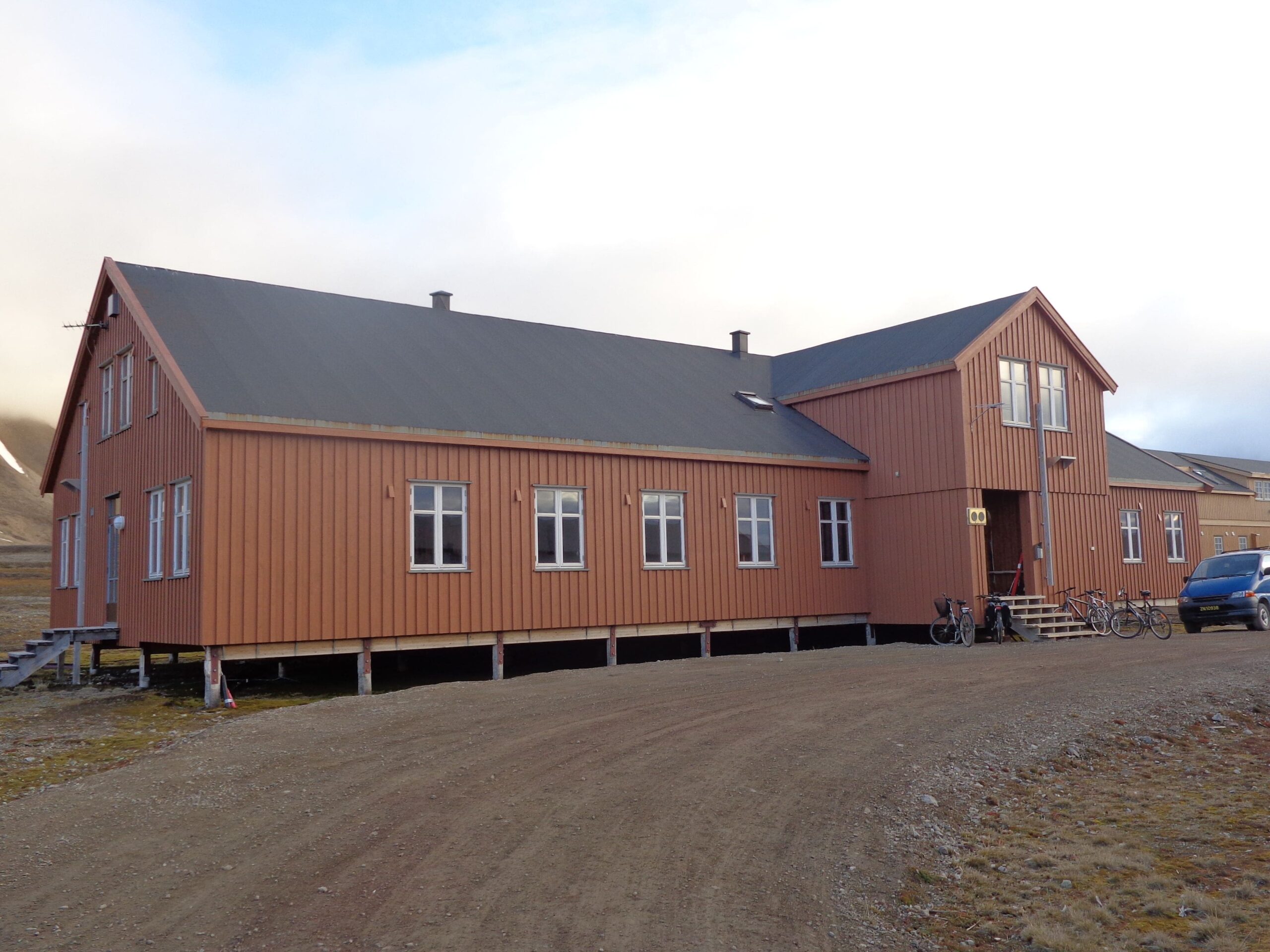 A two story woode house - Italian research station Stazione Dirigibile Italia in Ny-Ålesund - with a gravel road in front of it