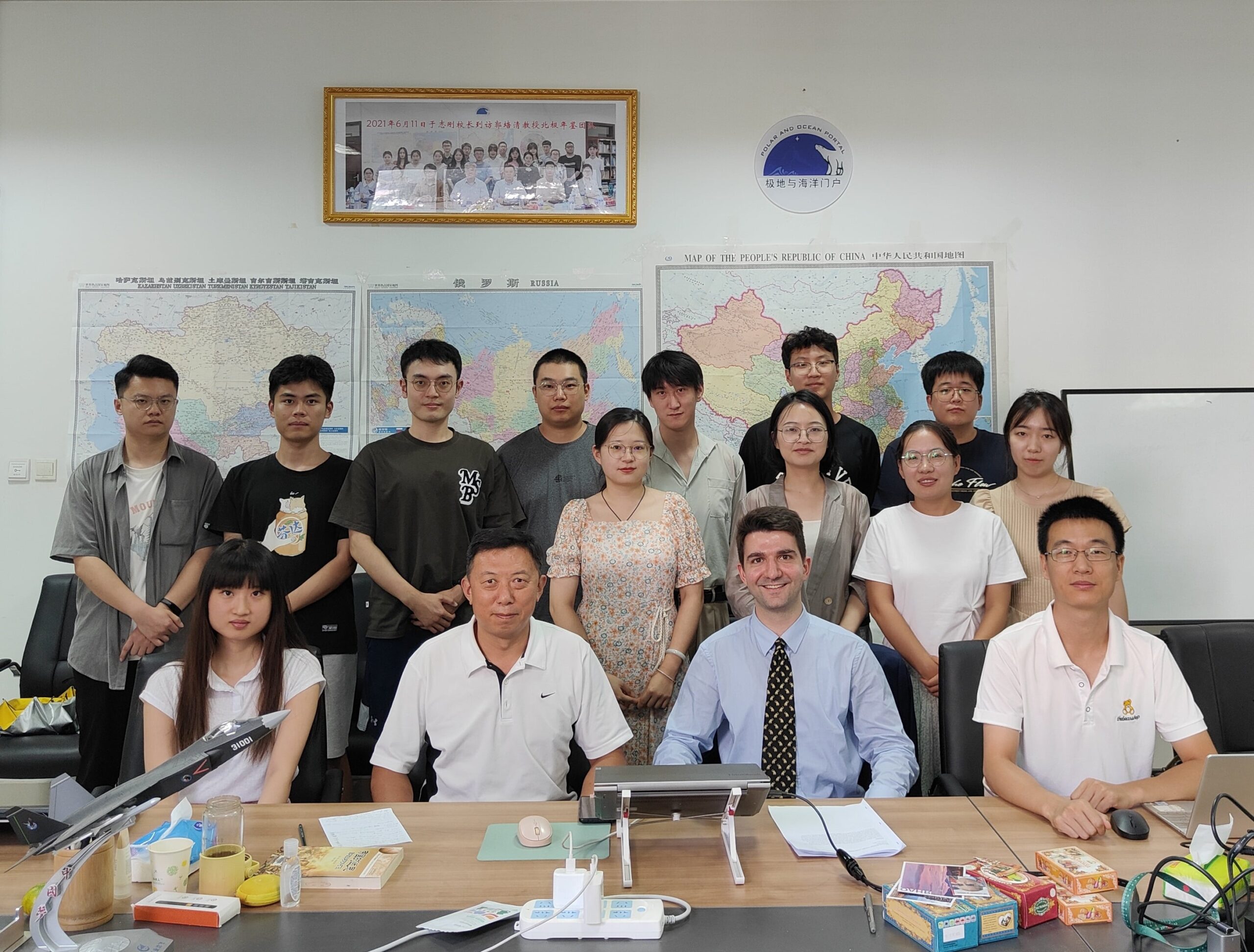 16 students and professors standing in front of maps, sitting at a table, in a classroom in China