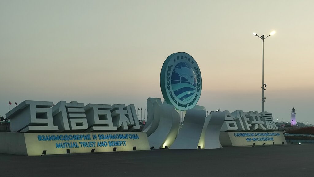 Shanghai Cooperation Organization logo and large Chinese characters, and Russian and English text reading Mutual Trust and Benefit, against a cloudy evening sky background