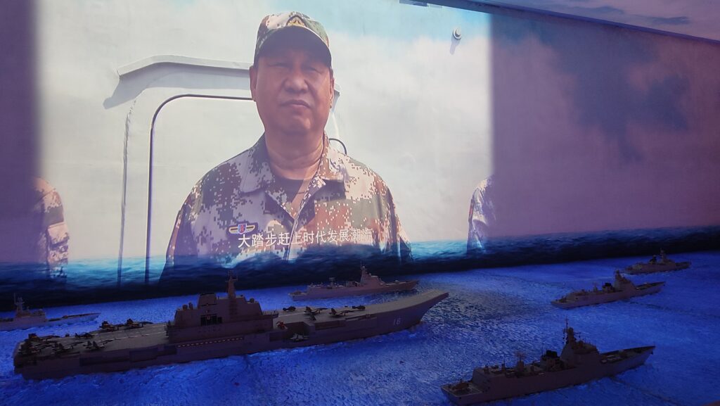 Projected image of Chinese President Xi Jinping in naval uniform in front of model Chinese navy ships in a museum exhibition
