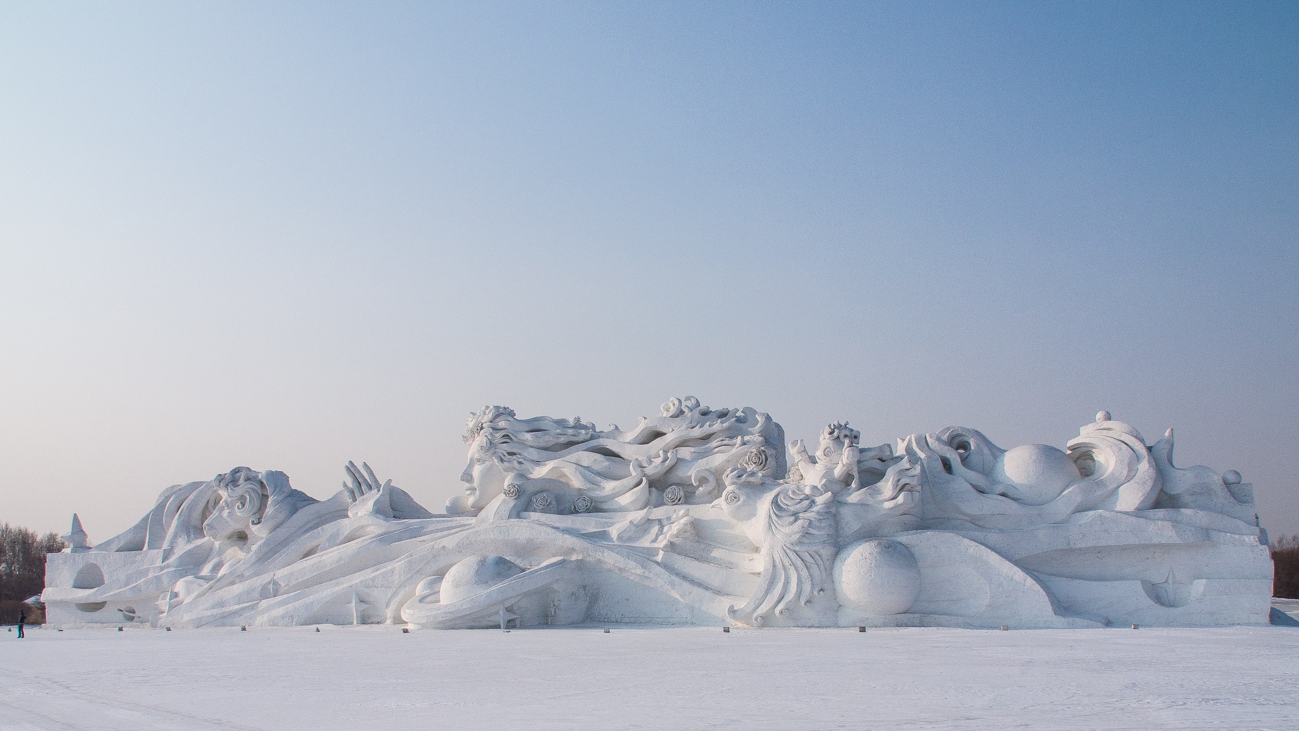 Snow sculptures depicting a woman’s head and animals with a light blue sky background from the Ice and Snow Festival in Harbin, northeast China