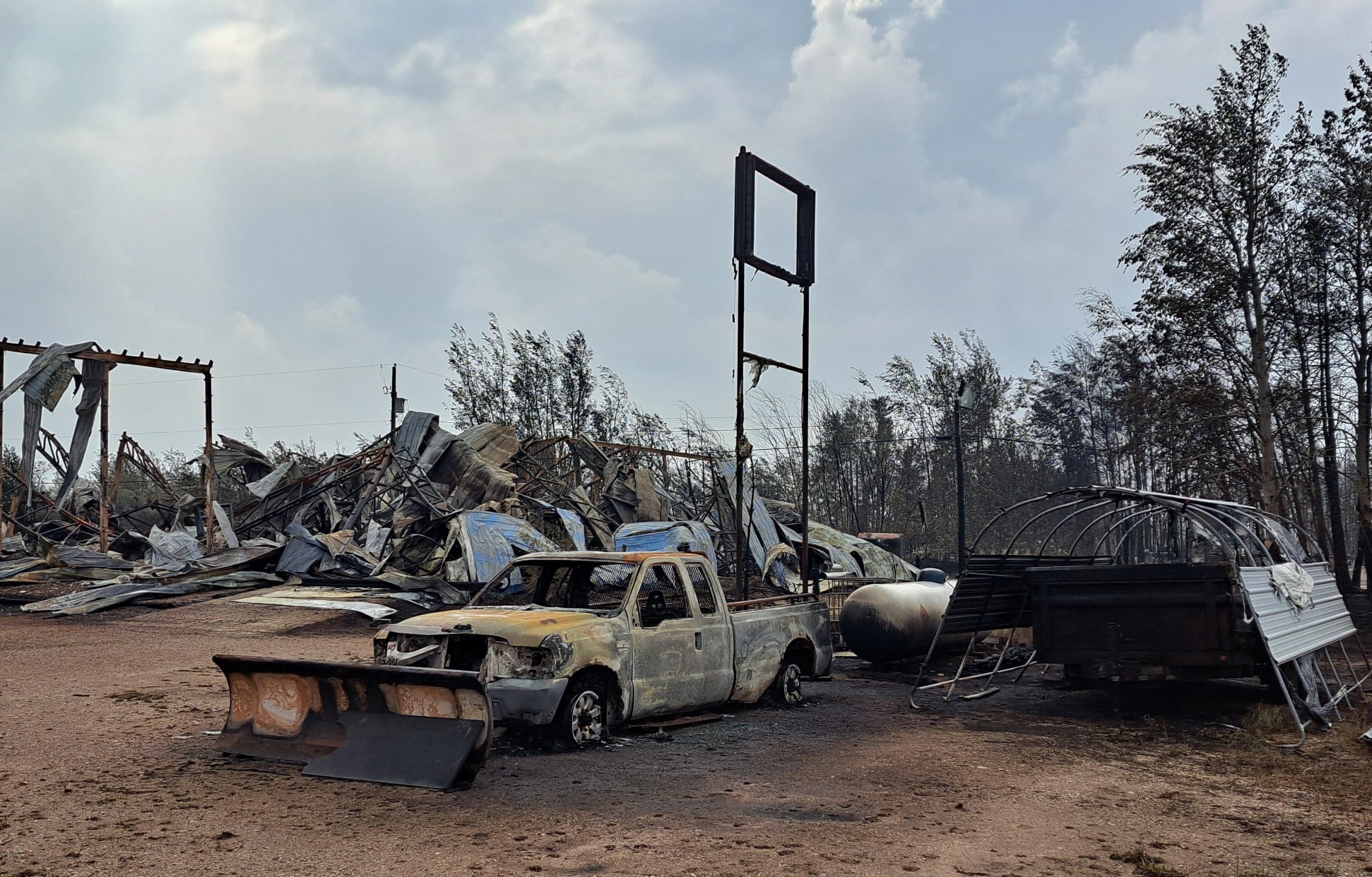 Enterprise, NWT after its fiery destruction last summer, burnt brown cars and homes are seen in the foreground against a smokey gray sky