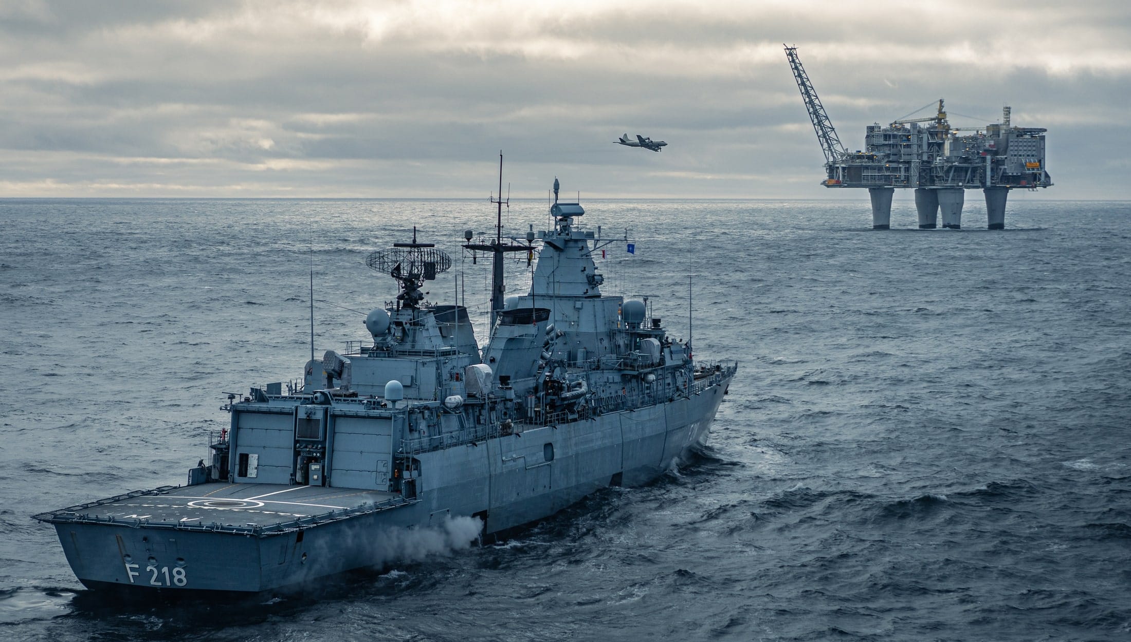 A large grey ship in dark water is seen in front of a grey natural gas platform in the sea