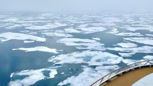 An expedition cruise ship sailing in the high latitudes in the Arctic Ocean, with sea ice at the front view