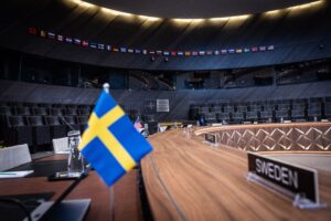 The yellow and blue Swedish flag is seen at the NATO headquarters against a brown conference table and dark blue background