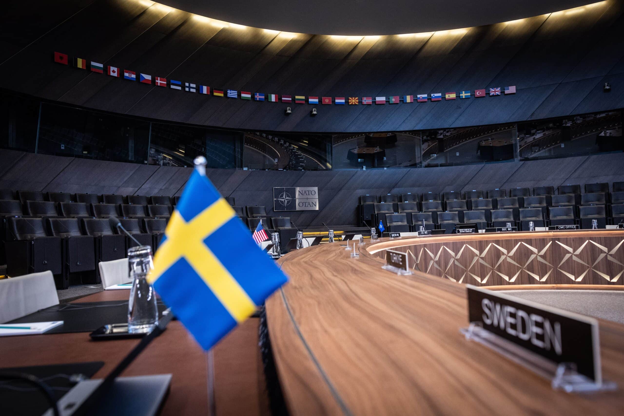 The yellow and blue Swedish flag is seen at the NATO headquarters against a brown conference table and dark blue background