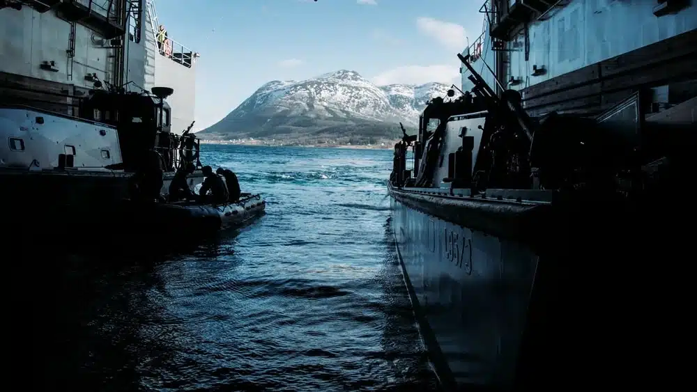 Two boats in dark blue water with a snowy mountain and pale blue sky in the background