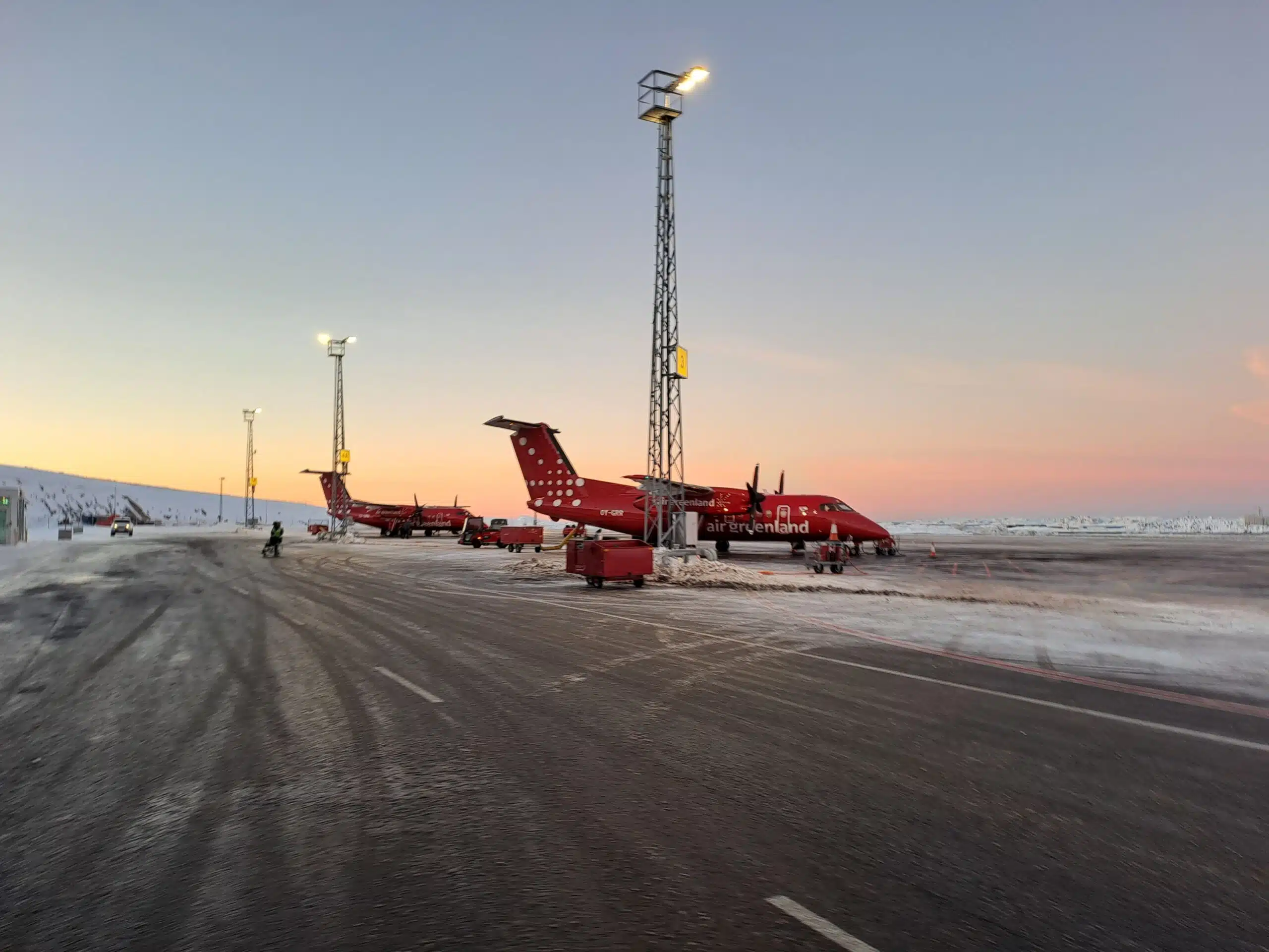 Two red airplanes on a tarmac with a sunset background