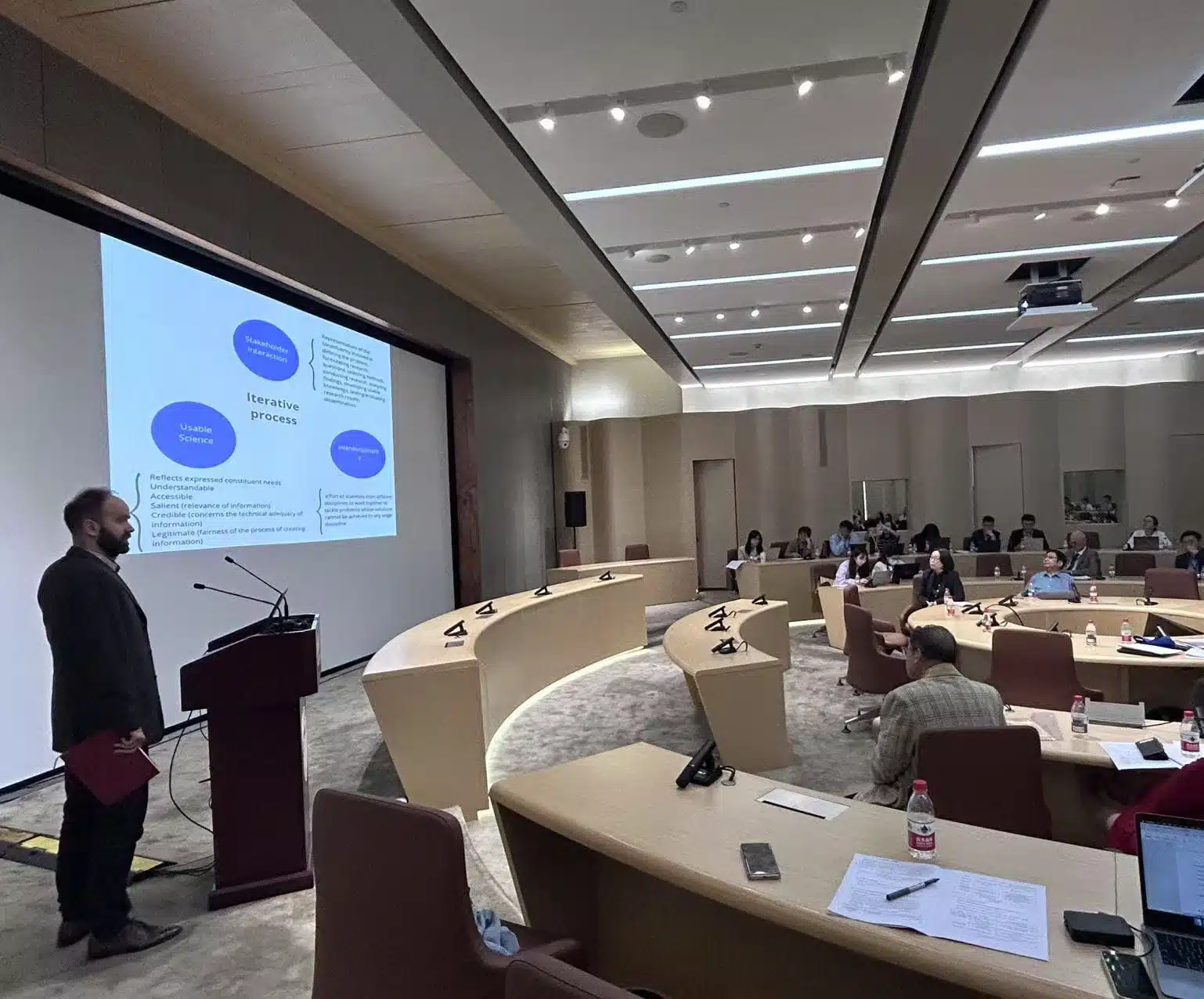 Scholar stands in front of powerpoint presentation as he presents to roundtable room at Tongji University in Shanghai, China