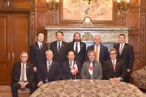 Group of officials in formal suits posing in a government meeting room, standing in a line with documents in hand, in an official indoor setting