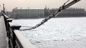 Snow-covered view of the Neva River in St. Petersburg, Russia, with historic buildings and a bridge with snow on the railing