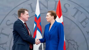 A man and a woman shake hands in front of two flags.