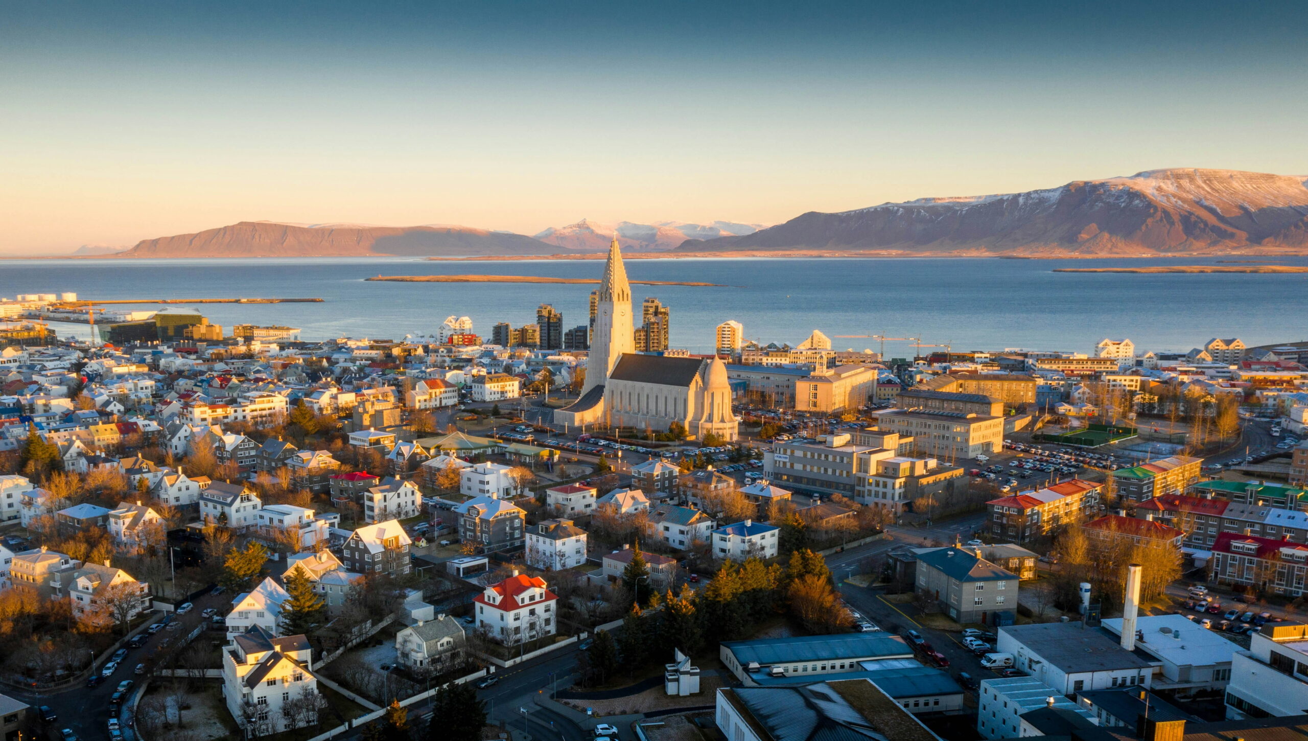 Aerial view of Reykjavík, Iceland, featuring Hallgrímskirkja church, colorful neighborhoods, Faxaflói Bay, and surrounding mountains