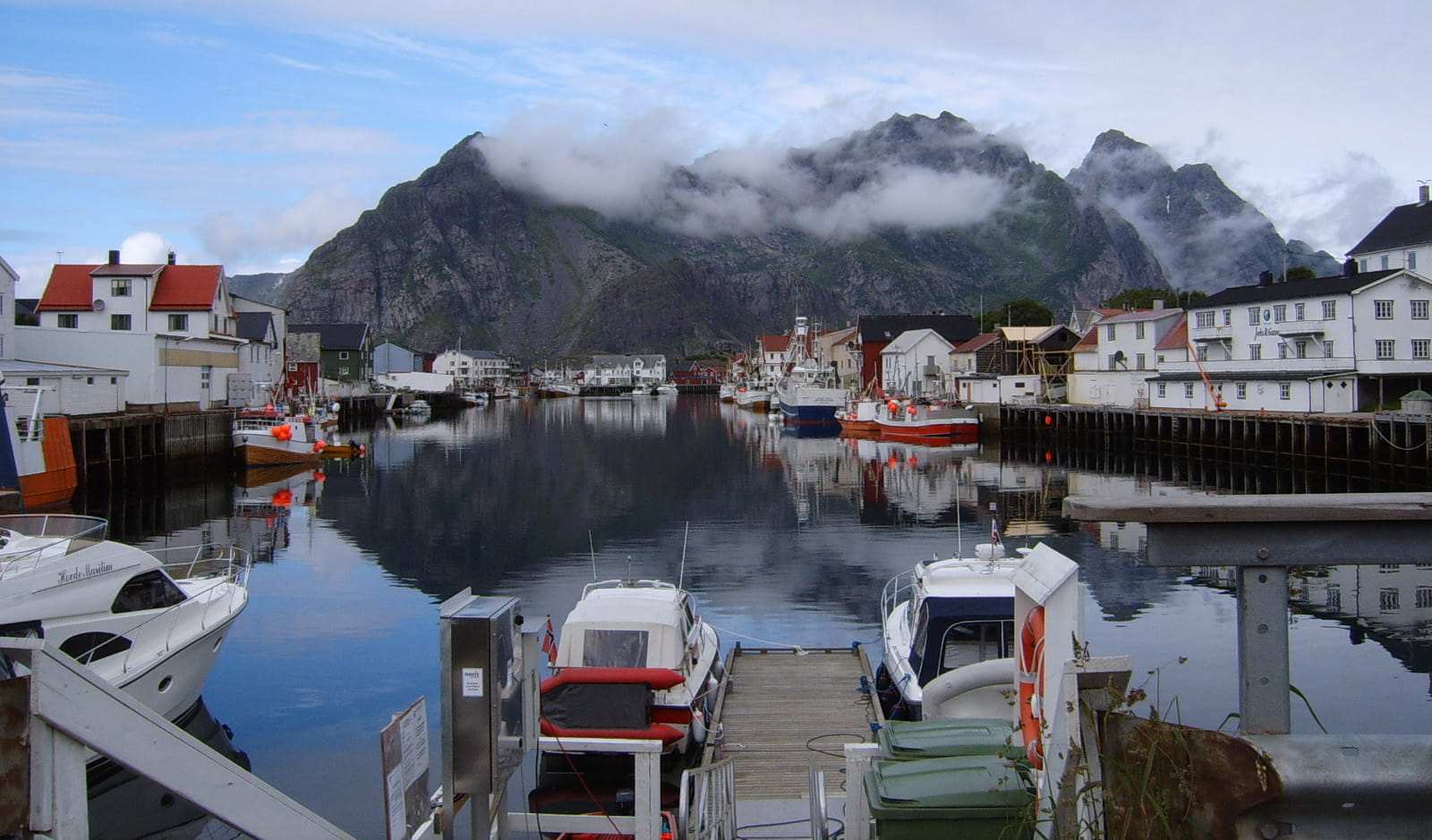 Fishing boats moored in Henningsvær harbour with steep, cloud-covered mountains behind them